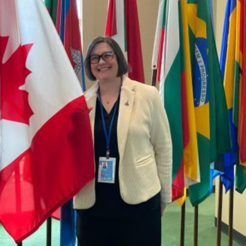 A woman in a white jacket stands with the Canadian flag at the United Nations